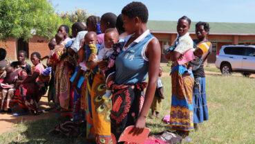 Mothers line-up and wait for their children to receive the malaria vaccine, Mkaka Primary School Outreach, Malawi