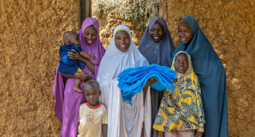 A mother her children hold a free mosquito net delivered to their household during a door-to-door mosquito distribution in Gabasawa, Kano, Nigeria