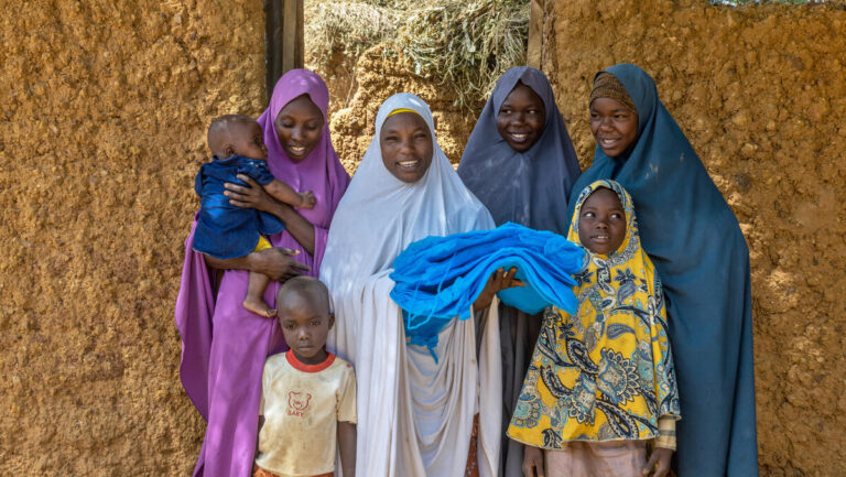 A mother her children hold a free mosquito net delivered to their household during a door-to-door mosquito distribution in Gabasawa, Kano, Nigeria