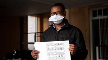 A patient with drug-resistant TB is holding up a pill packet which contains the tablets he takes to treat the TB.